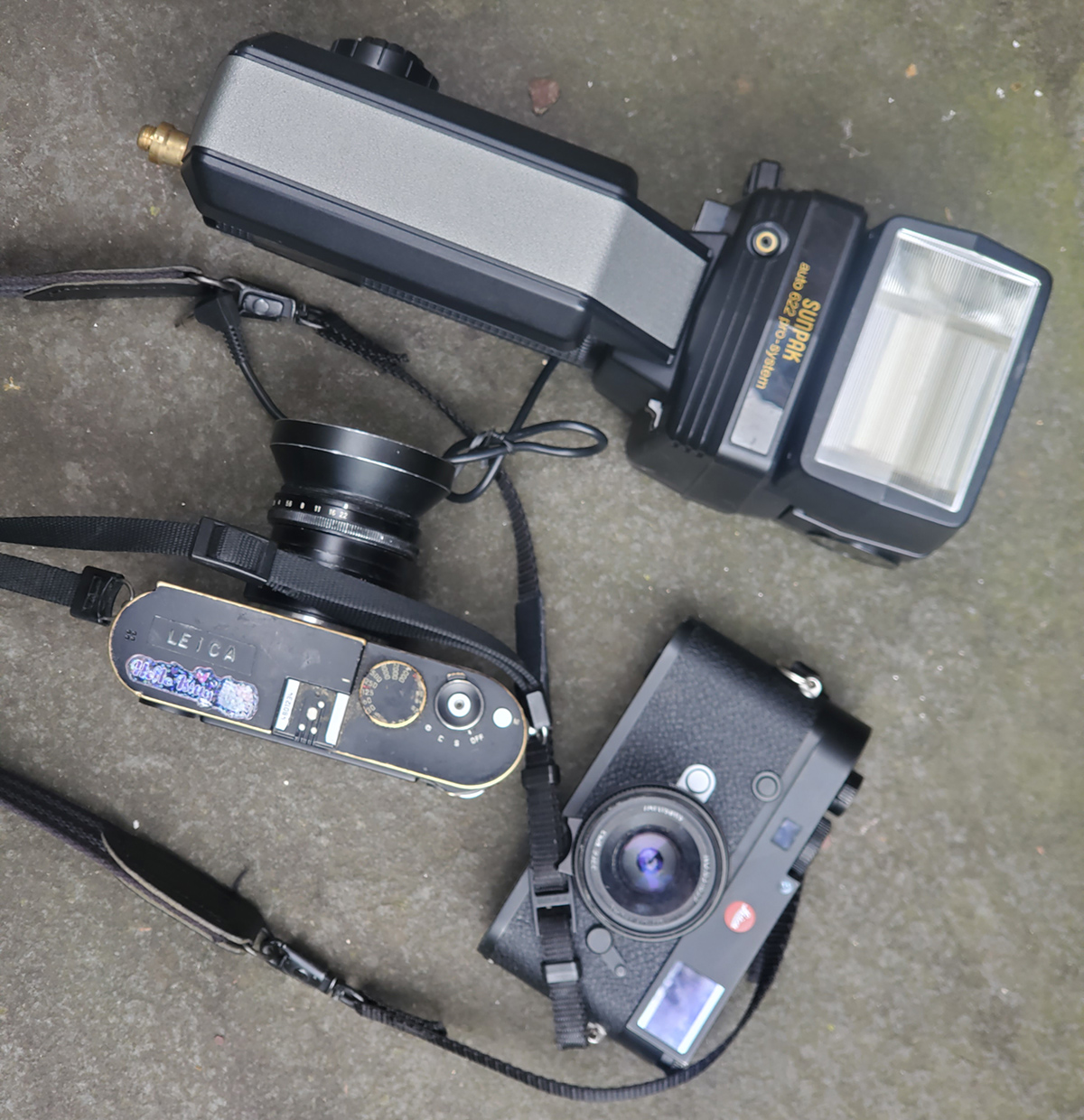 two small cameras and a large flash lying on the ground